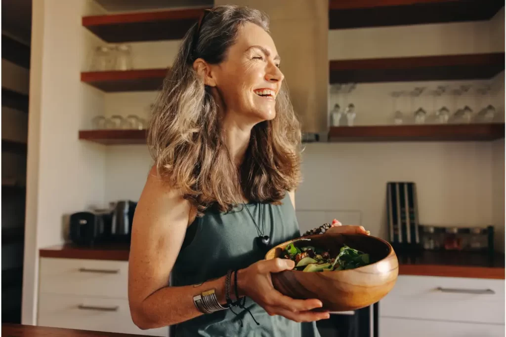 Integrative Prevention Hero image showing a smiling woman in a kitchen hold a bowl of salad